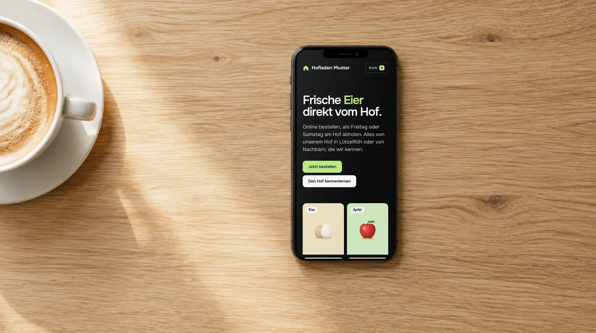 Phone next to a cup of coffee, showing the demo website Hofladen Muster